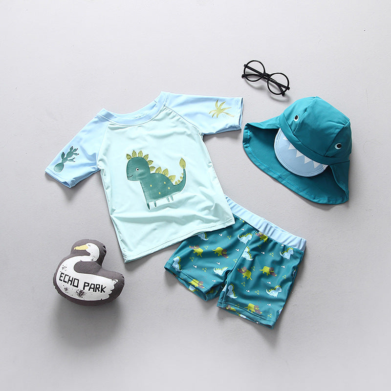 Boys dinosaur swimming suit featuring a dinosaur graphic, paired with shorts, sunglasses, and a matching hat.